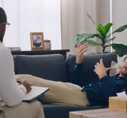 Man on sofa consulting psychologist in therapy, healthcare clinic and medical office for mental hea