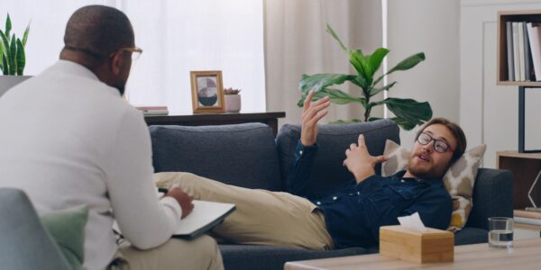 Man on sofa consulting psychologist in therapy, healthcare clinic and medical office for mental hea