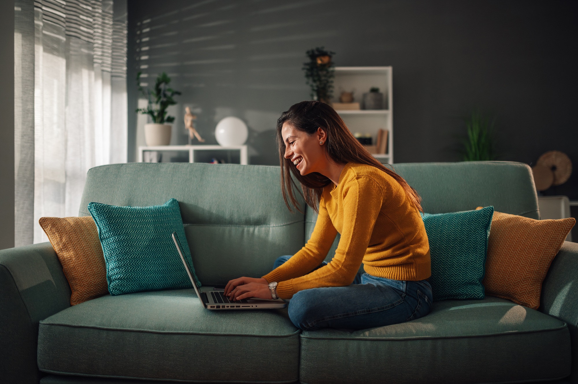 Smiling woman using laptop and checking email while sitting on the couch at home